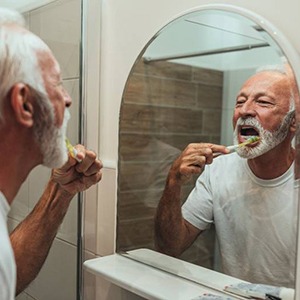 man brushing his teeth to care for dental implants in Alhambra