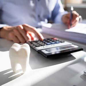 Man at desk pressing calculator with paperwork and large model tooth