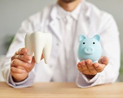 Man in white coat holding model tooth in one hand and piggy bank in the other