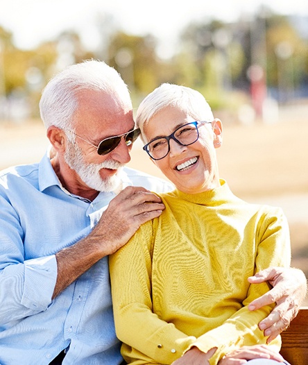 An older couple seated on an outdoor bench and smiling after receiving All-On-4 in Alhambra