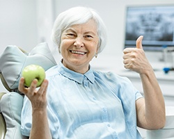 woman with dental implants smiles and holds an apple