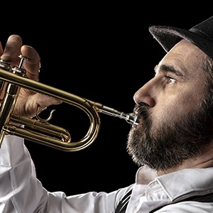 A man with a beard and fedora playing the trumpet without his Invisalign aligners