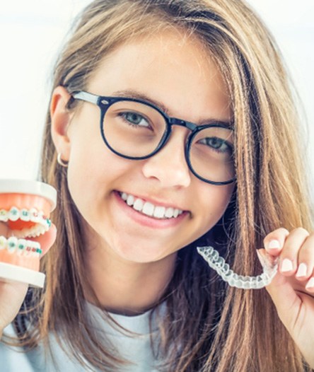 teen smiling and holding a model of braces in one hand and an Invisalign aligner in the other