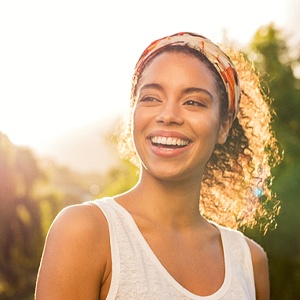 A woman wearing a headband and white tank top smiling after completing treatment with Invisalign