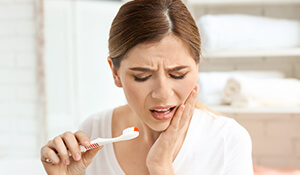 Woman with tooth brush holding cheek