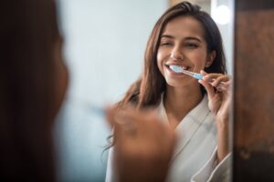 a patient smiling while brushing her teeth