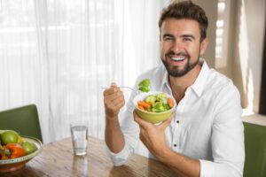 Man smiling while eating a bowl of vegetables